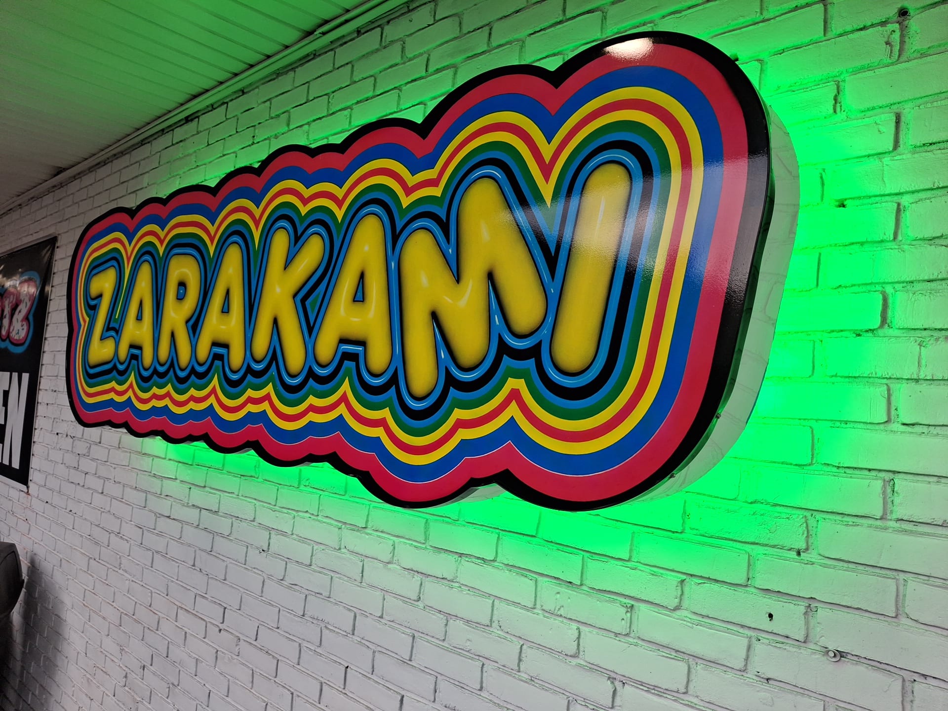 Angled view of the halo-lit ZARAKAMI cabinet sign with green glow on brick
