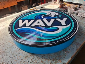 Round WAVY cabinet sign resting face-up on a shop workbench