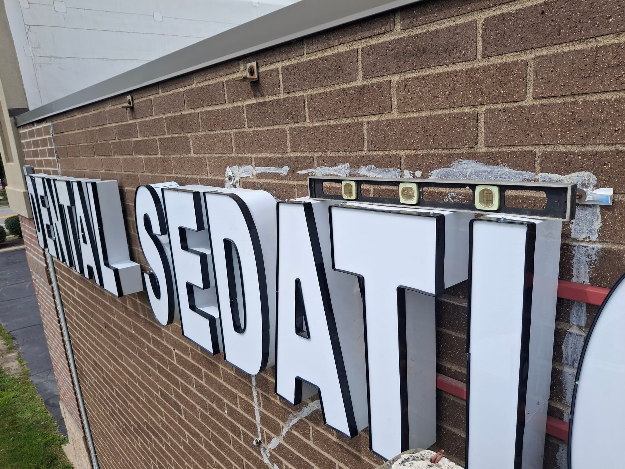 White channel letters and a level clamped to a brick wall during sign installation