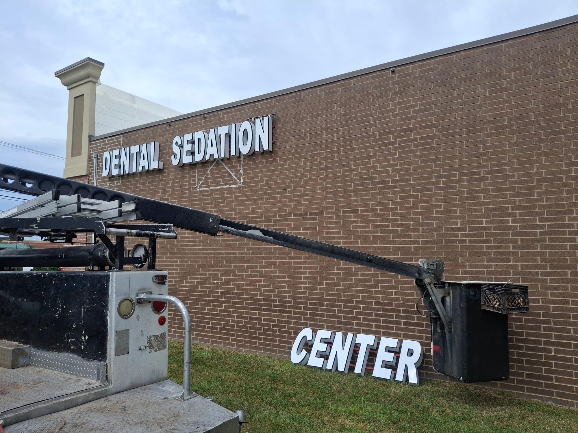 DENTAL SEDATION CENTER channel letters going up on a brick wall beside a bucket truck boom