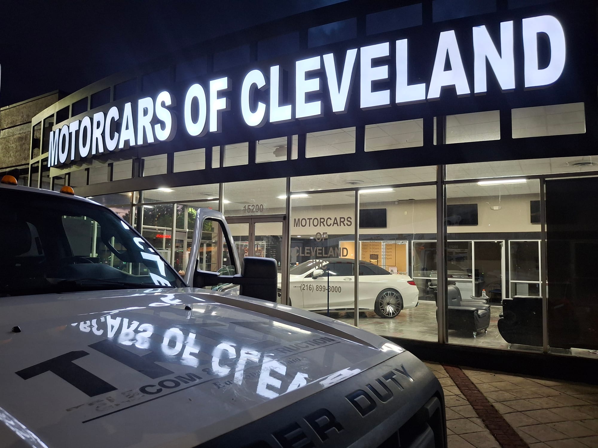 Illuminated MOTORCARS OF CLEVELAND channel letters glowing above a dealership at night