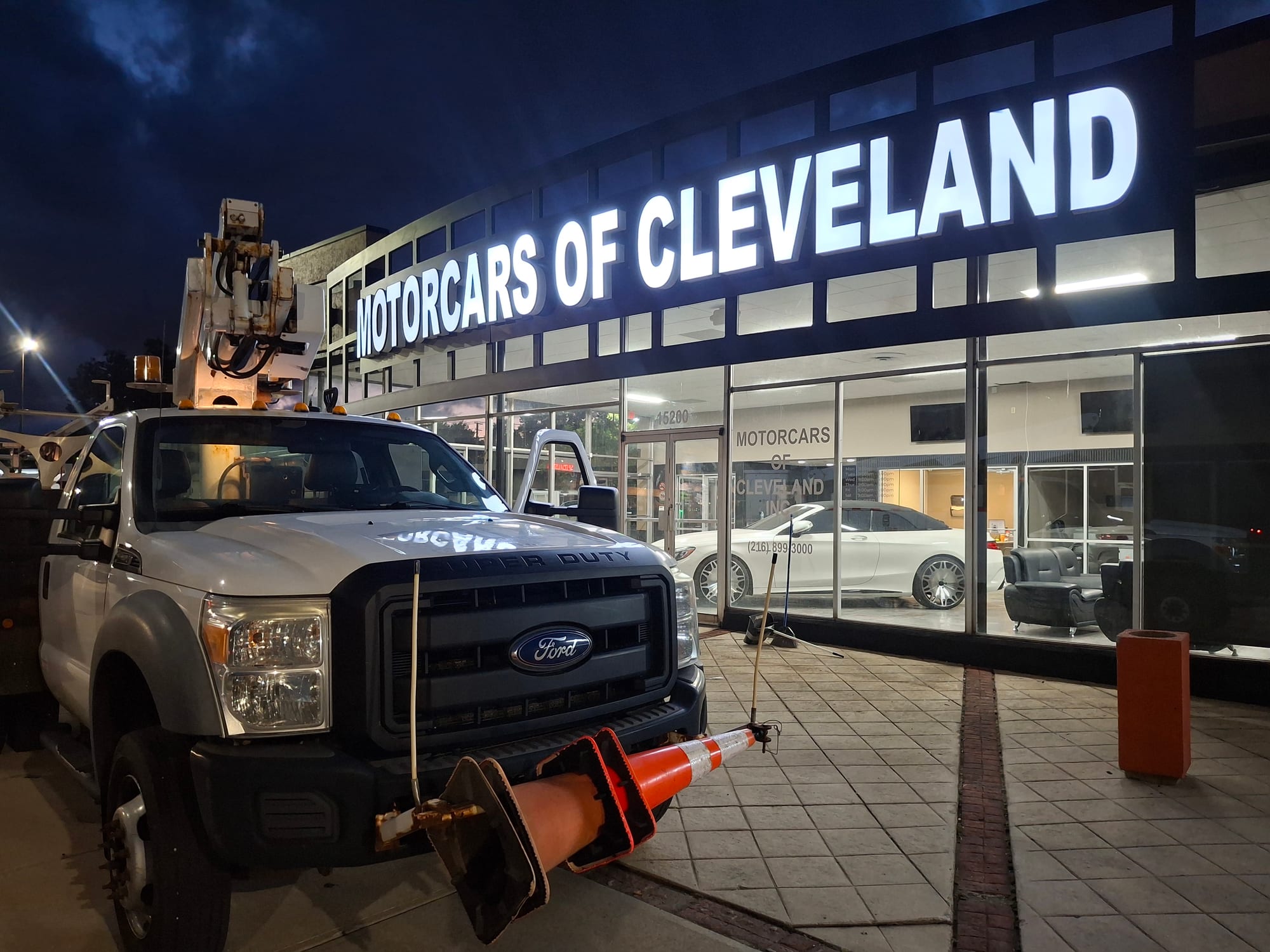 Lit MOTORCARS OF CLEVELAND channel letters at night with a bucket truck parked below