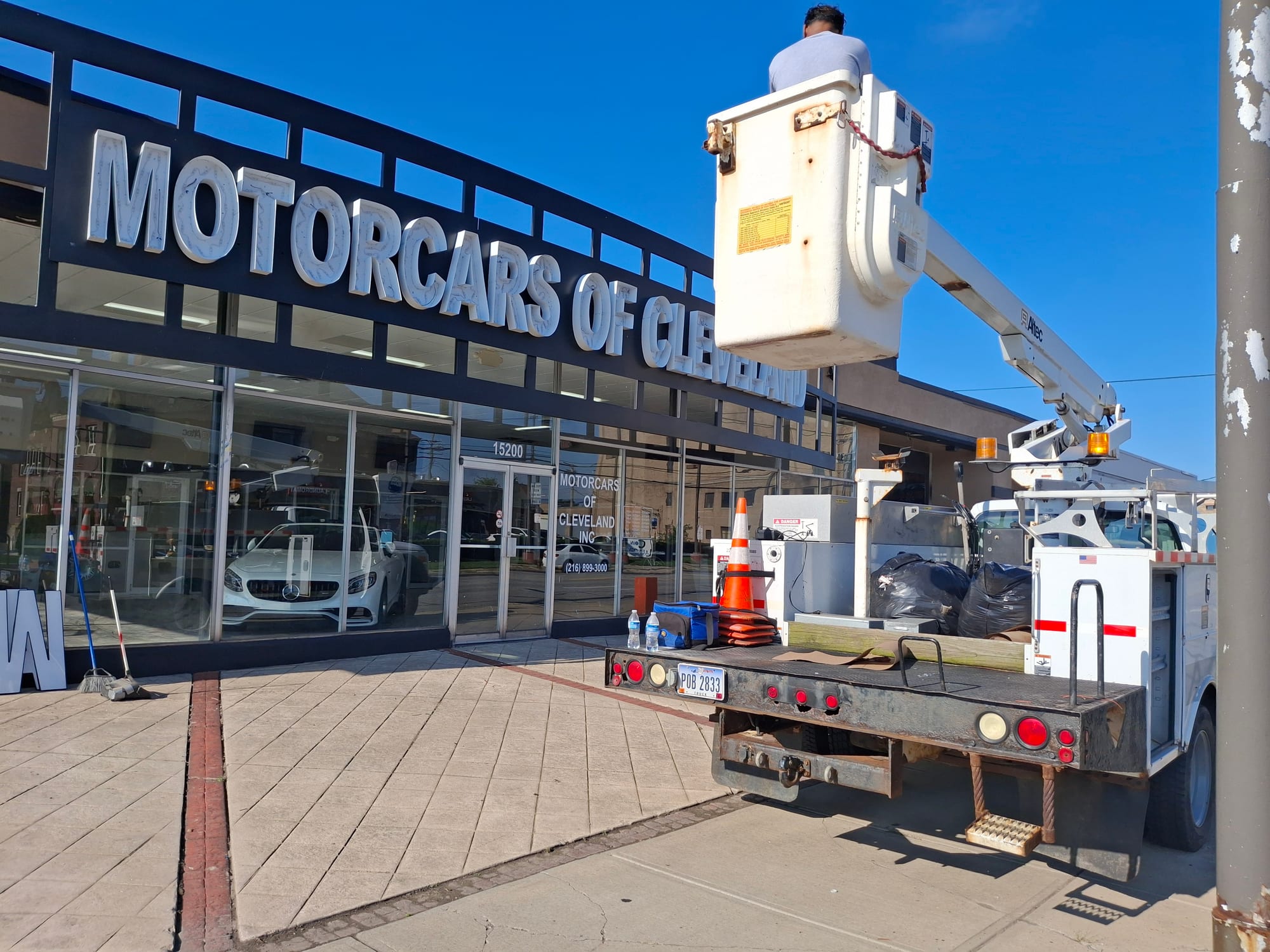 Worker in a bucket lift working on MOTORCARS OF CLEVELAND letters above a dealership