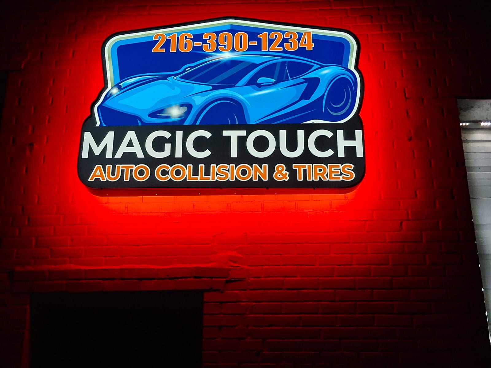 Illuminated MAGIC TOUCH AUTO COLLISION & TIRES cabinet sign glowing red on a brick wall