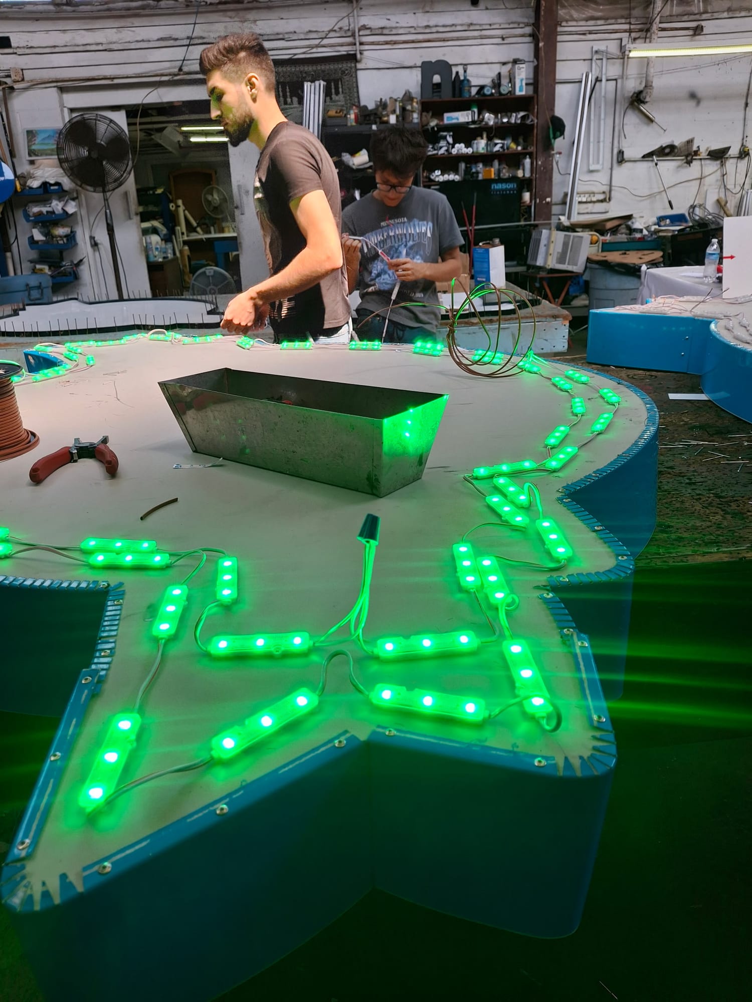 Two workers wiring green LED modules into a large star-shaped sign in the shop