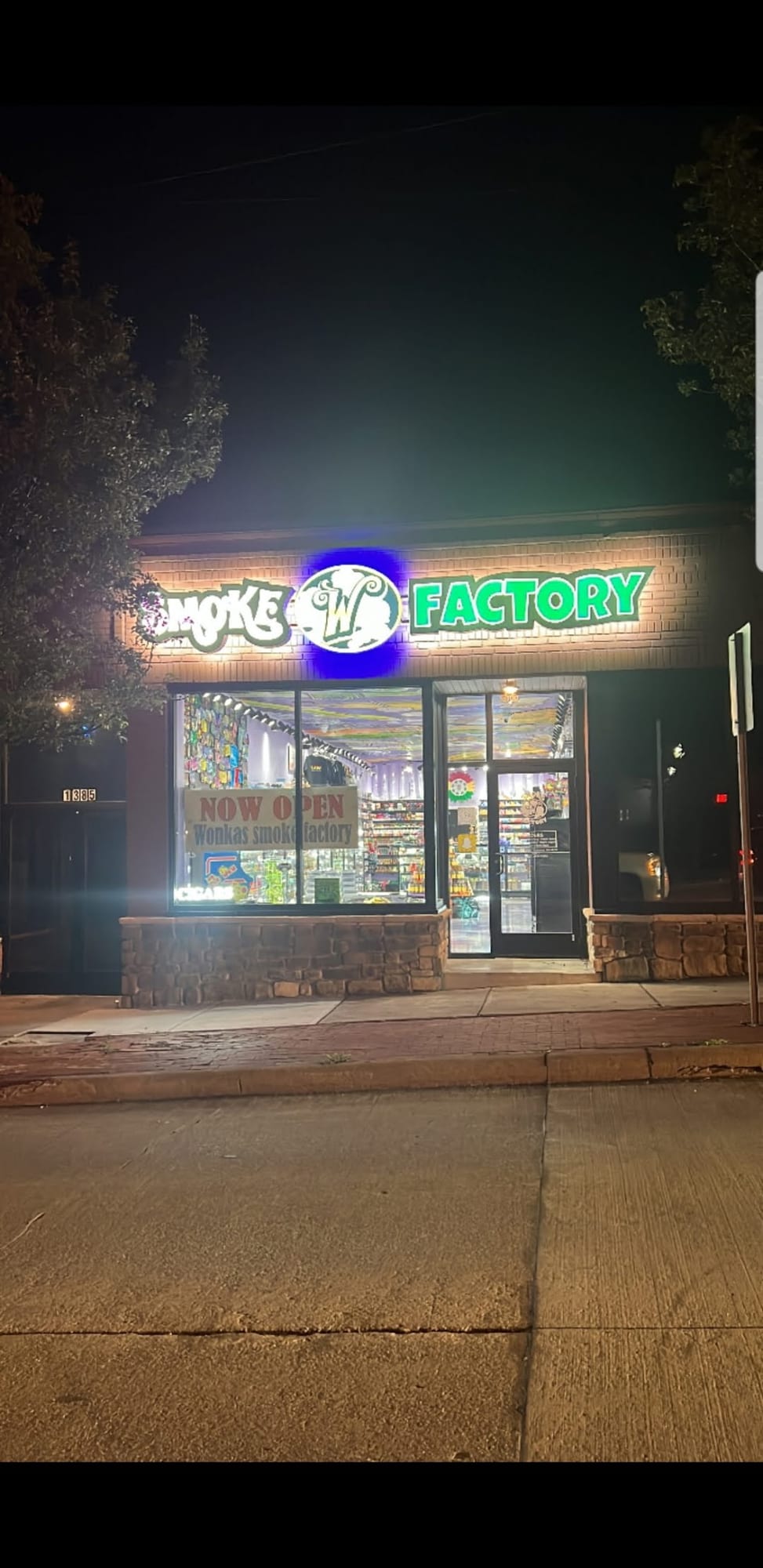 Lit SMOKE FACTORY sign above a storefront at night with a Now Open window banner