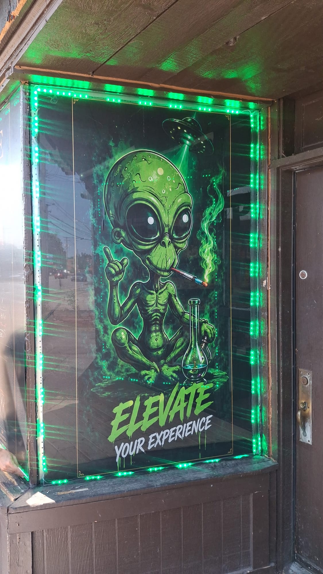 Printed alien window graphic reading ELEVATE YOUR EXPERIENCE framed by green LED lights