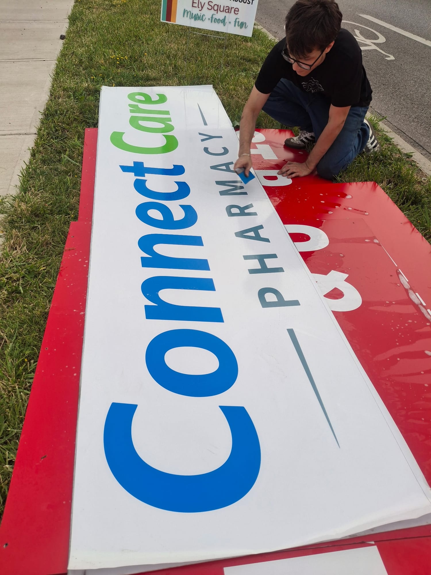 Worker squeegeeing printed Connect Care Pharmacy vinyl onto a sign panel outdoors