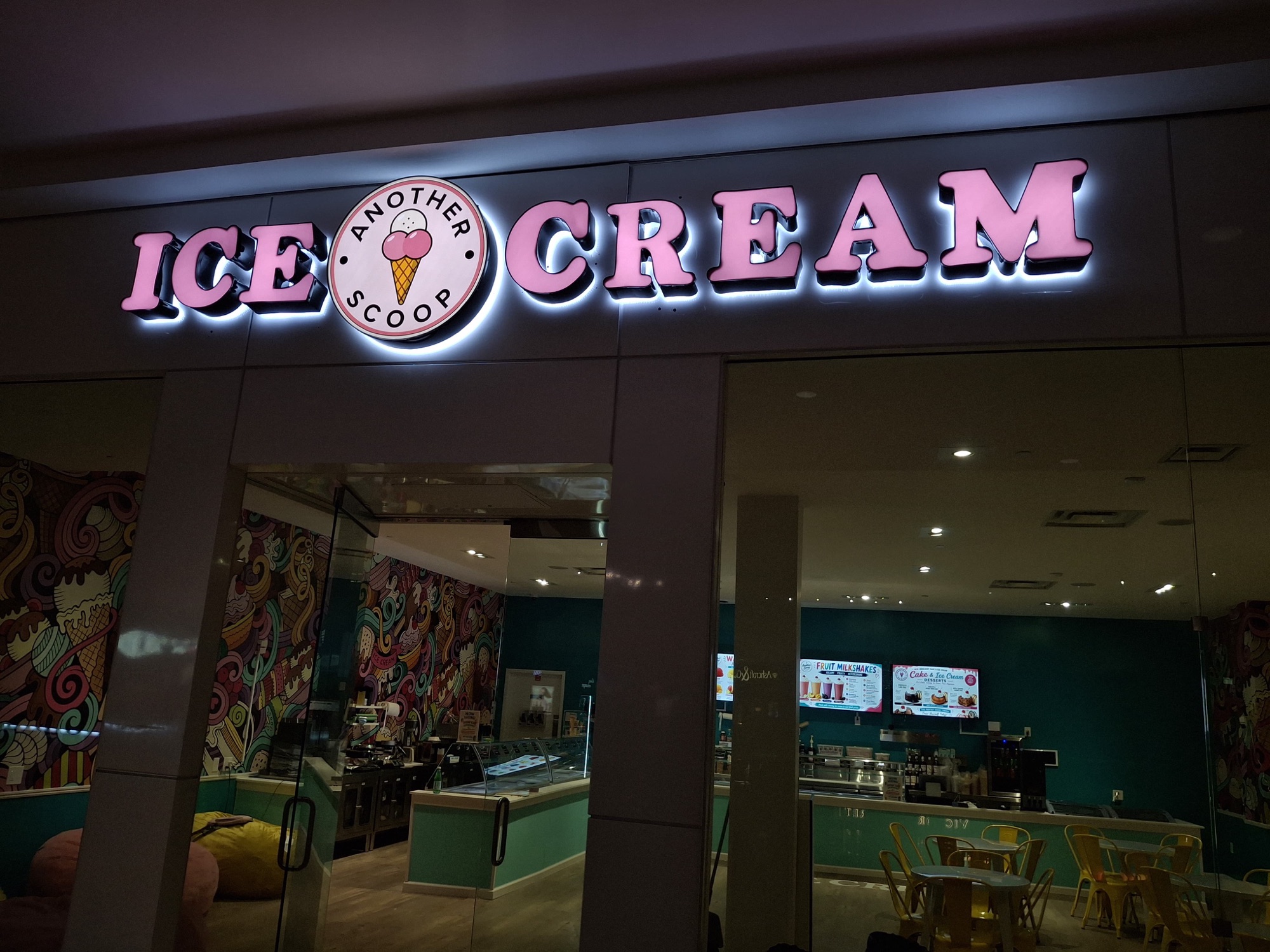 Pink halo-lit ICE CREAM channel letters with the Another Scoop medallion above the storefront